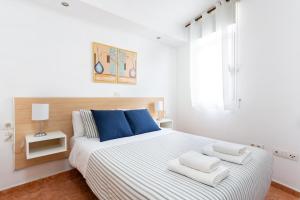 a white bedroom with a large bed with blue pillows at Apartamentos Ohana - Edificio Tonillo in Los Cristianos