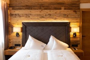 a bed with white pillows and a wooden wall at Olympia-Relax-Hotel Leonhard Stock in Finkenberg