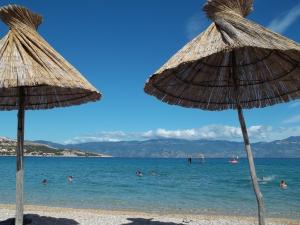 two straw umbrellas on a beach with people in the water at Lovrić Apartments in Baška