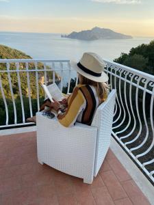 a woman sitting in a chair reading a book on a balcony at Acquamarina Accommodation in Massa Lubrense