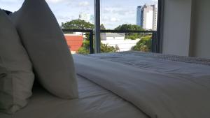 uma cama com lençóis brancos e almofadas em frente a uma janela em START Villa Morra Rent Apartments em Assunção