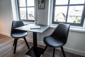 a table and two chairs in a room with two windows at Het Vergulde Visje in Den Burg