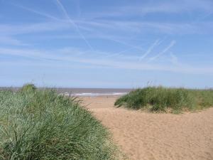 a sandy beach with grass and the ocean in the background at Luxury Holiday Home in Anderby Creek in Anderby