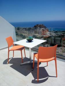 2 sillas naranjas y una mesa blanca en el balcón en Bouganville Bed & Breakfast Stegna en Archangelos