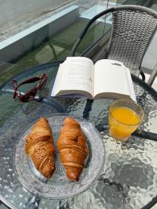 a glass table with a plate of croissants and an open book at Perla Hotel Halkidiki in Kallithea Halkidikis