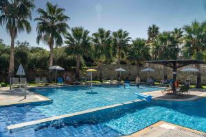 a large swimming pool with palm trees in the background at Almyrida Village & Waterpark in Almyrida