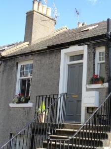 una casa gris con una puerta azul y escaleras en Peebles Cottage Apartment with River View and Bike Store en Peebles