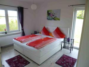een wit bed met rode kussens in een kamer met ramen bij Ambiente in Westerholz