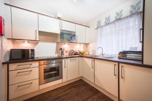 cocina con armarios blancos, fregadero y microondas en The Knight Residence by Mansley, en Edimburgo