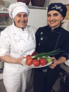 two women in a kitchen holding a plate of vegetables at Oksamit Resort in Vorokhta
