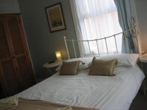 a bed with white sheets and pillows in front of a window at The Beeches in Clacton-on-Sea