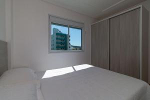 Habitación blanca con cama y ventana en Aluguel Apartamento 2 quartos vista mar Bombas/SC, en Bombinhas