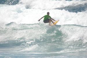 un hombre montando una ola en una tabla de surf en el océano en A.I.R. Villa Marinedda, en Isola Rossa