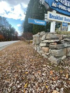 Yankee Trail Motel في Holderness: علامة على الشارع وجدار حجري بجانب طريق