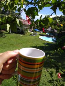 een persoon met een koffiekopje voor een tuin bij Flat Village Paraíso da Lua in Pipa
