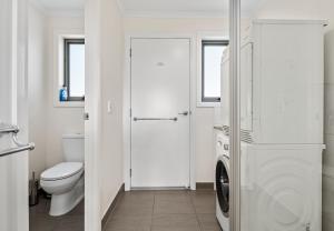 a white bathroom with a toilet and a washer and dryer at GRANITE BEACH HOUSE @ Bay of Fires in Binalong Bay