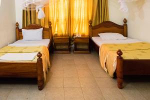 two beds sitting in a room with yellow curtains at Palm world Hotels Mbarara in Mbarara