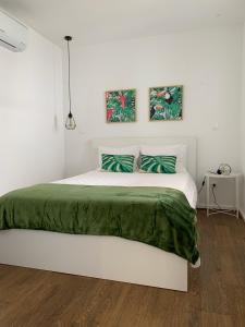 a white bedroom with a large bed with green sheets at Belém Lodge in Ponta Delgada