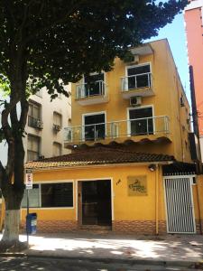 ein gelbes Gebäude mit einem Balkon und einem Baum in der Unterkunft Caminho do Mar Hotel in Guarujá