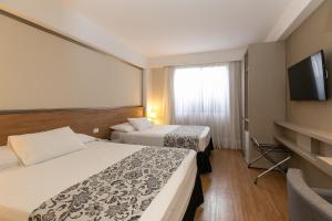 フォス・ド・イグアスにあるビアレ カララタス ホテル ＆ イベントスのベッド2台、薄型テレビが備わるホテルルームです。