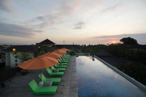 a pool with chairs and umbrellas on top of a hotel at Zest Legian by Swiss-Belhotel International in Legian