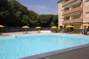 a swimming pool with chairs and umbrellas next to a building at Acquasmeralda appartamento 01 in Rosolina Mare