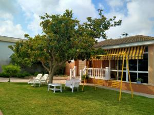 a playground in front of a house with a tree and chairs at Chalet con piscina privada en Vinaròs in Vinarós