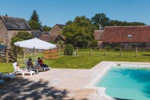 dos personas sentadas bajo un paraguas junto a una piscina en Le gîte d'Etienne en Joué-du-Bois