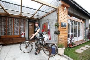 uma mulher ao lado de uma bicicleta em frente a uma casa em Old Mamaboy Marines Hostel獨立包棟三間雙人雅房 em Kaohsiung