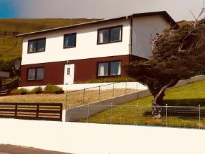a house behind a fence with a tree at The Atlantic view guest house, Sandavagur, Faroe Islands in Sandavágur