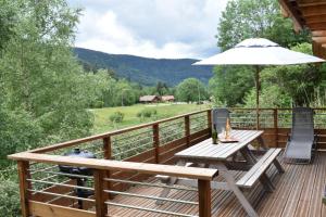 una terraza de madera con mesa de picnic y sombrilla en Le Chardonneret, en La Bresse