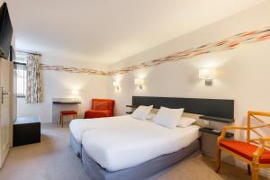 a hotel room with a white bed and a chair at Hotel Restaurant Le Dauphin et Le Spa du Prieuré in Caen