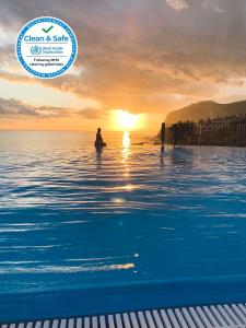 eine Person, die bei Sonnenuntergang im Wasser des Ozeans steht in der Unterkunft Apartment Formosa - Infinity pool in Funchal