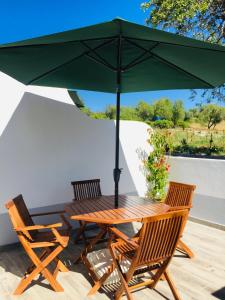 una mesa de madera y sillas bajo una sombrilla verde en Quinta dos Netos, en Tavira