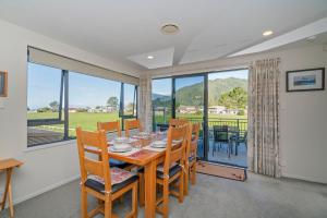 a dining room with a table and chairs and windows at Pauanui Hangar Retreat - Pauanui Holiday Home in Pauanui