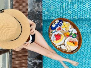 a woman wearing a hat next to a pool with a bowl of food at Sofiana My Khe Hotel & Spa- Rooftop Pool Bar in Danang