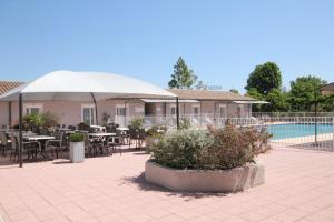 a patio with tables and chairs and a white umbrella at Hôtel Saint Louis in Le Thor