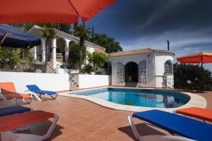 a swimming pool with chairs and umbrellas next to a house at Villa Andalucia in Cómpeta