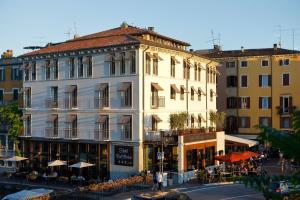 a large white building with tables and umbrellas on a street at Hotel Bell'arrivo by Dori in Peschiera del Garda