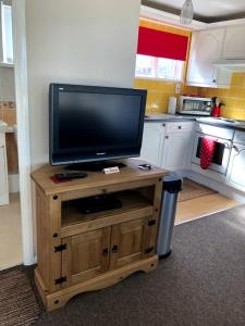 a television on a wooden stand in a kitchen at Broadside Chalet Park No 90 in Norwich