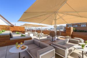 - un toit-terrasse avec des chaises, des tables et un parasol dans l'établissement Melia Madrid Serrano, à Madrid