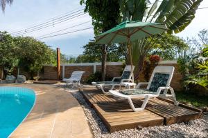 duas cadeiras e um guarda-sol ao lado de uma piscina em Pousada Recanto das Palmeiras em Ubatuba