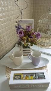 een tafel met twee kopjes en een dienblad met paarse rozen bij Angellina Apartmani in Sremska Mitrovica