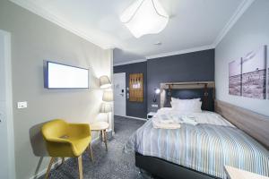 a bedroom with a bed and a yellow chair at Strandhotel Duhnen in Cuxhaven