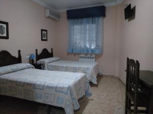 Habitación con 2 camas y ventana con cortinas azules. en Hostal El Polígono, en Lucena