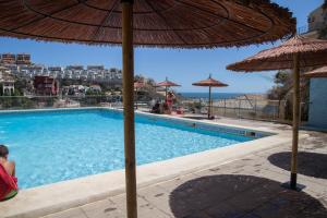 a woman sitting under an umbrella next to a swimming pool at Big Terrace Apartment Cullera in Cullera
