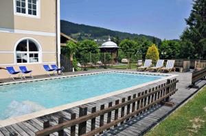 a swimming pool with blue chairs and a house at Alpen Hotel Eghel Resort & SPA in Folgaria