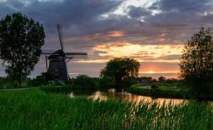 wiatrak i rzeka z zachodem słońca w tle w obiekcie Mondriaanmolen, a real Windmill close to Amsterdam w mieście Abcoude