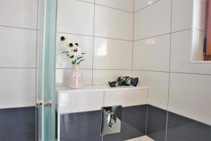 a white tiled bathroom with a vase of flowers on a shelf at Iva Apartmani in Vodice