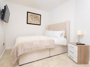 a white bedroom with a bed and a night stand at Valdeni Apartments in Leeds